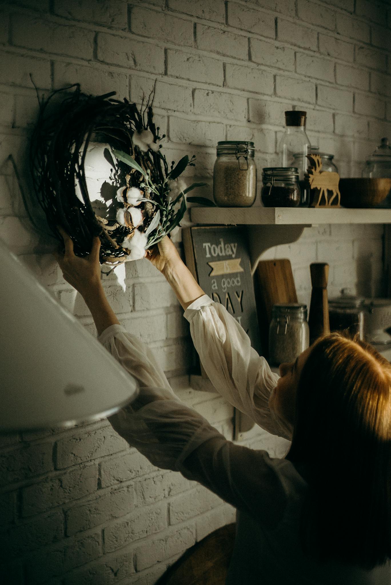 A woman places a wreath on a brick wall, creating a cozy holiday atmosphere indoors.